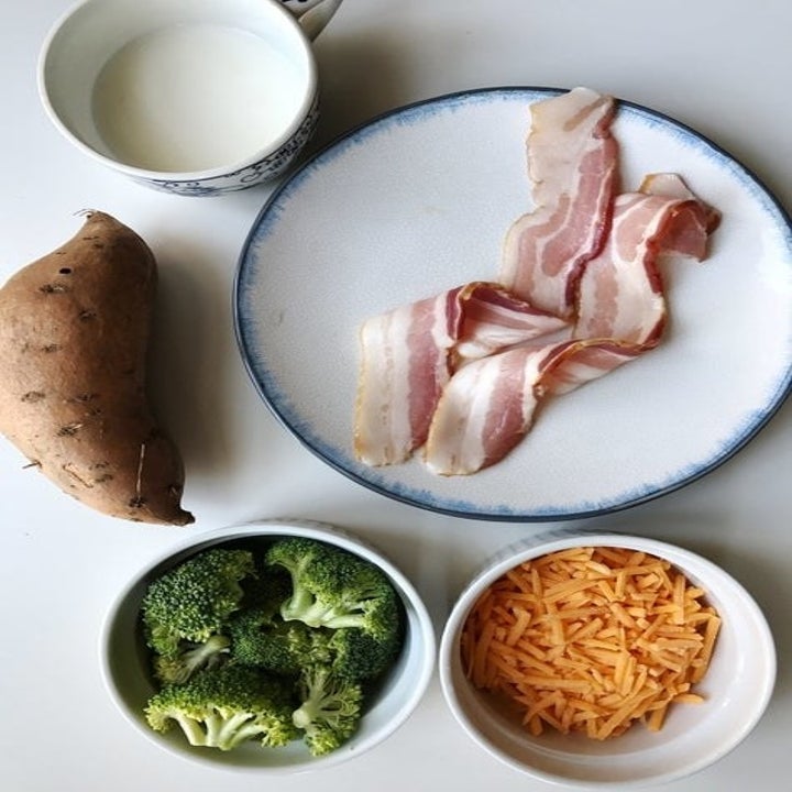 Ingredients on a countertop including a sweet potato, broccoli, shredded cheese, and bacon.