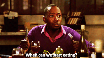 Winston from &quot;New Girl&quot; with silverware in hand at the dinner table, eager to eat.