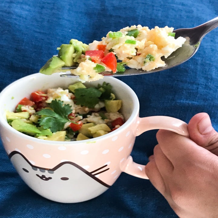 A mug full of scrambled eggs with vegetables and a fork taking a bite.