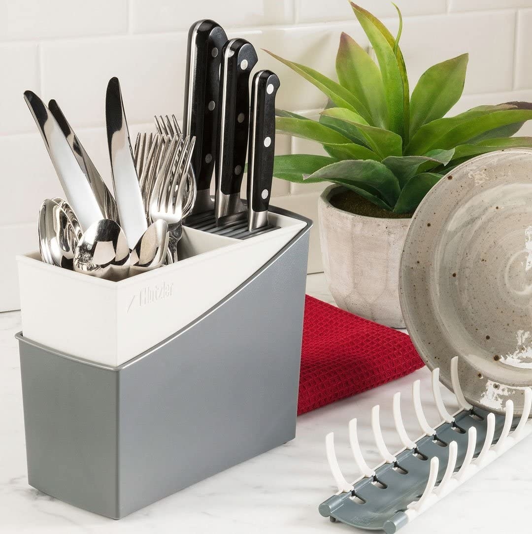 A fully loaded cutlery drainer on a countertop next to some clean dishes
