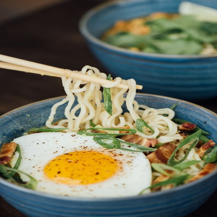 A bowl of ramen with scallions, bacon, and a fried egg.