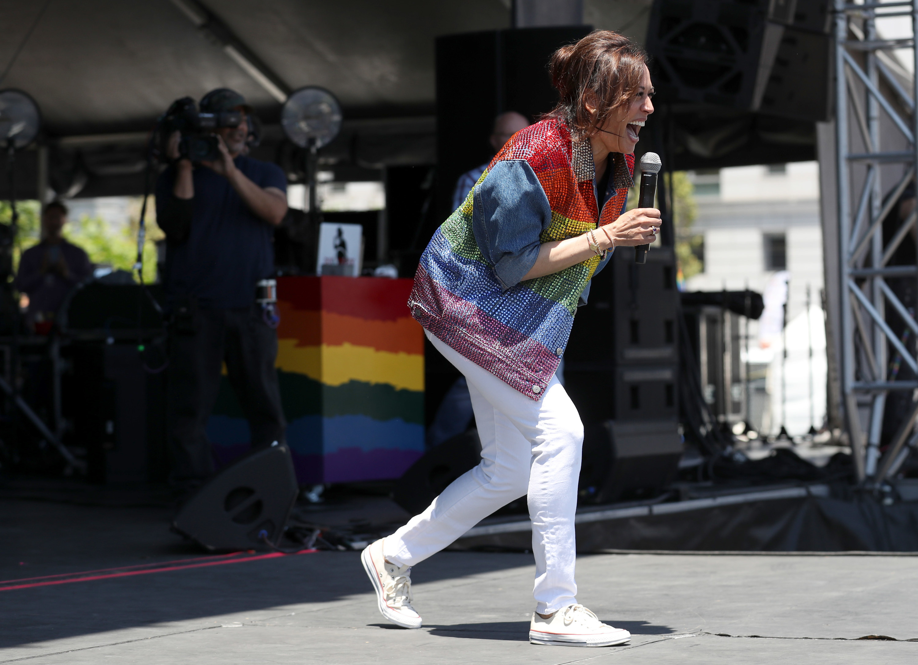 Kamala Harris, wearing white Converse sneakers and a rainbow denim jacket, speaking at Pride parade in San Francisco.