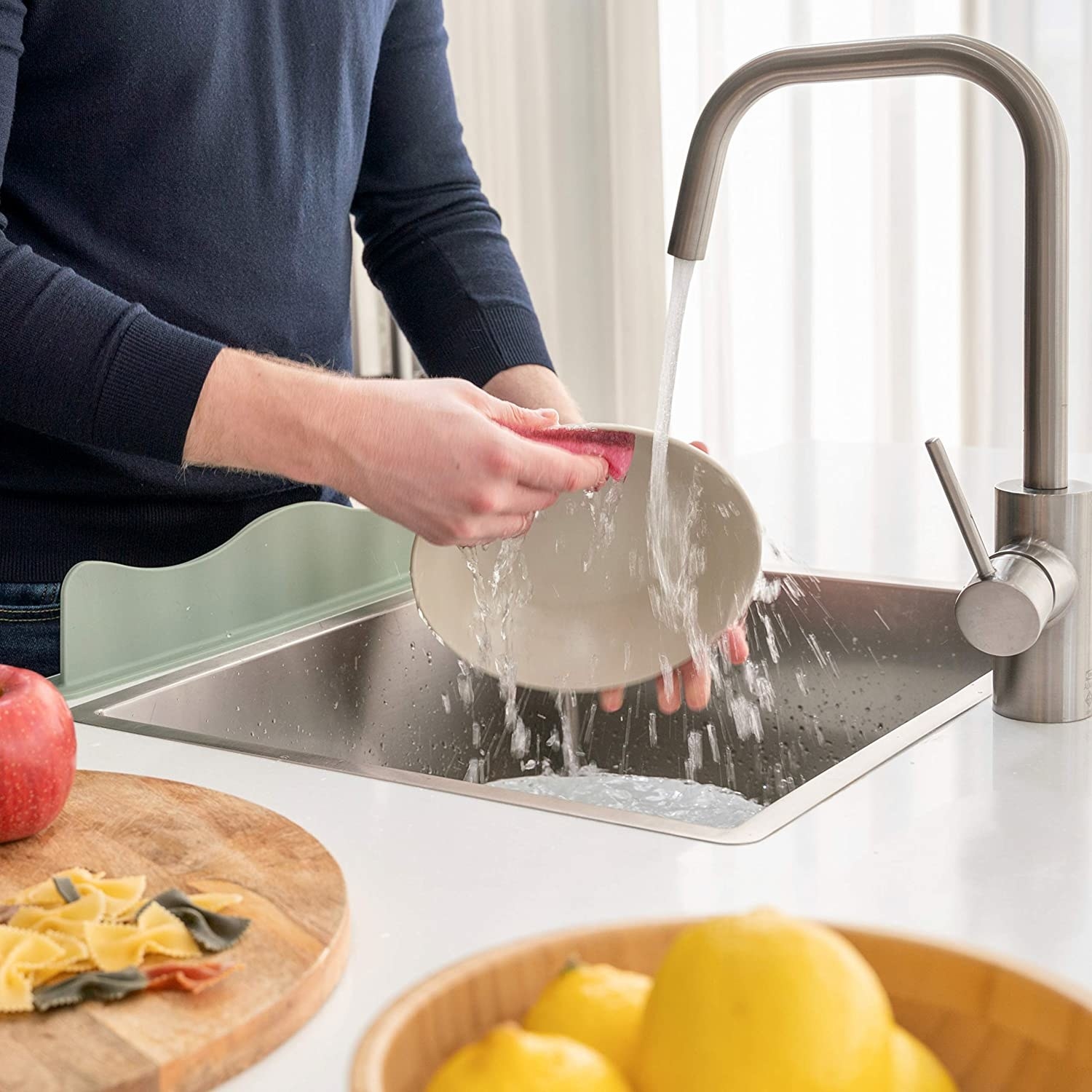A person washing dishes with the plash guard attached to their sink