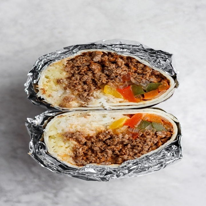 A burrito wrapped in foil, cut in half and stuffed with rice, ground beef, peppers, and cheese.