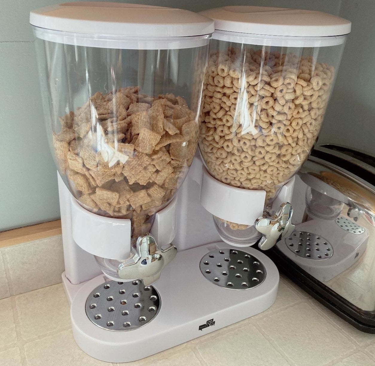 reviewer's white and clear cereal dispenser with silver knobs on their kitchen counter  