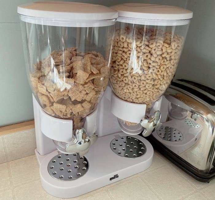 reviewer&#x27;s white and clear cereal dispenser with silver knobs on their kitchen counter  