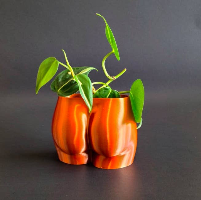 3D-printed copper booty-shaped pot with green plant inside