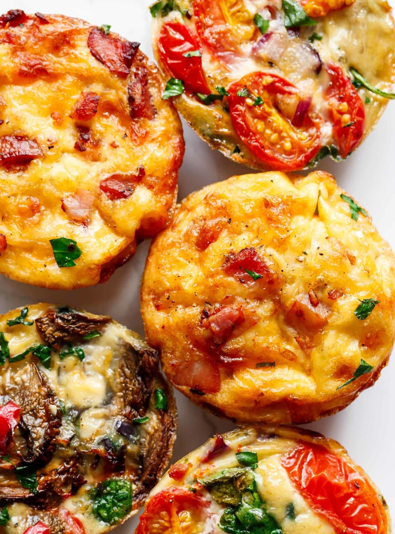 Five egg muffins filled with different veggies like tomato, spinach, mushroom, and pepper.