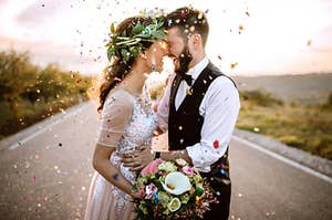 A man and woman in their wedding outfits surrounded by colorful confetti