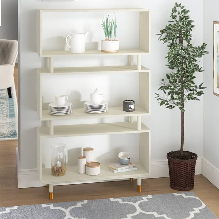 a white bookshelf with three big shelves, two smaller shelves between them, and gold legs