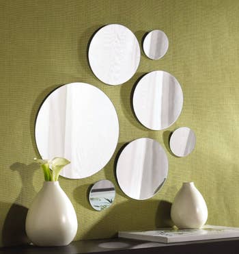 Set of seven big and small circle-shaped mirrors hanging on a green wall above a table