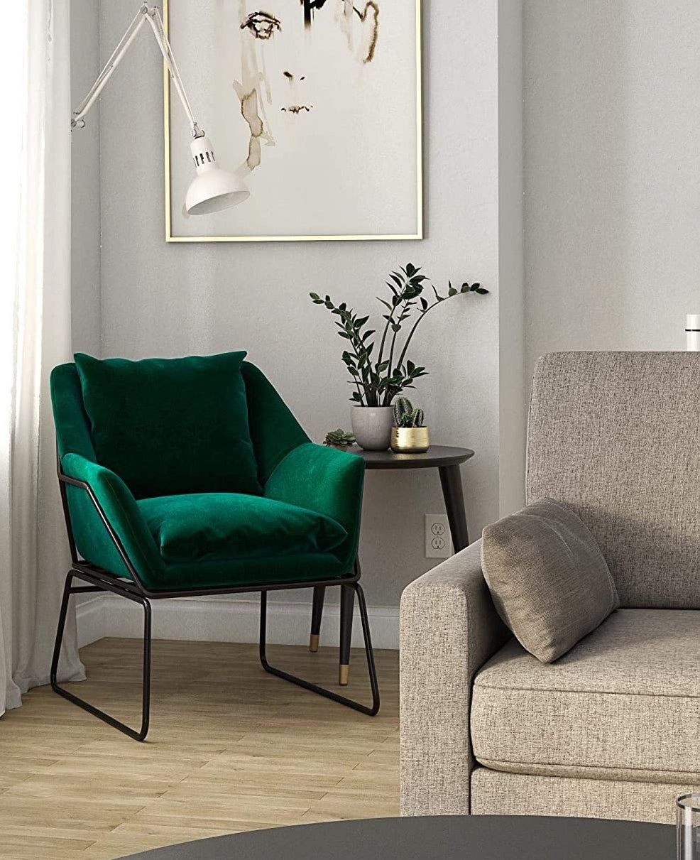 Green velvet chair with back pillow and black metal frame in a living room. 