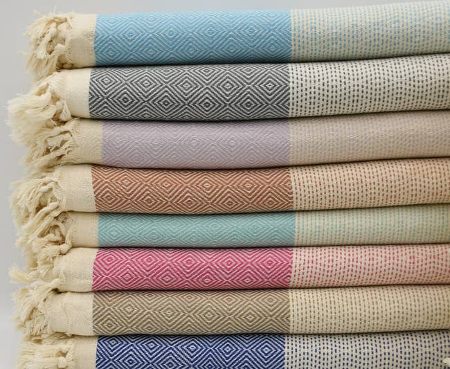 a stack of patterned blankets in different colors with fringed edges