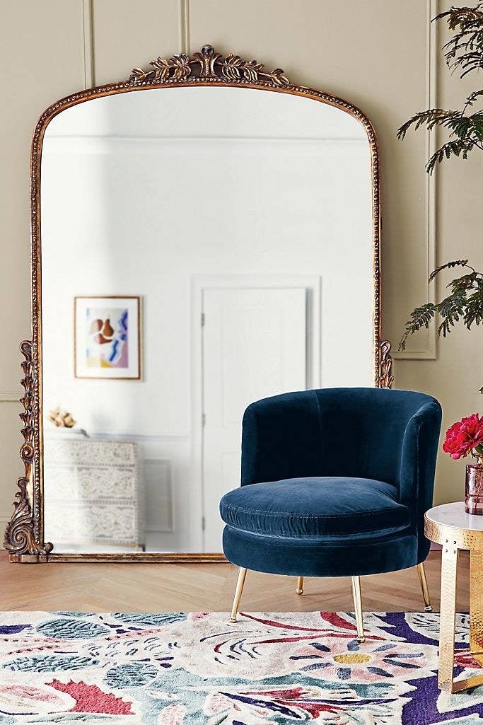 Wide floor-length mirror with a rounded top and gold frame with jeweled adornments on the top middle and bottom side edges.