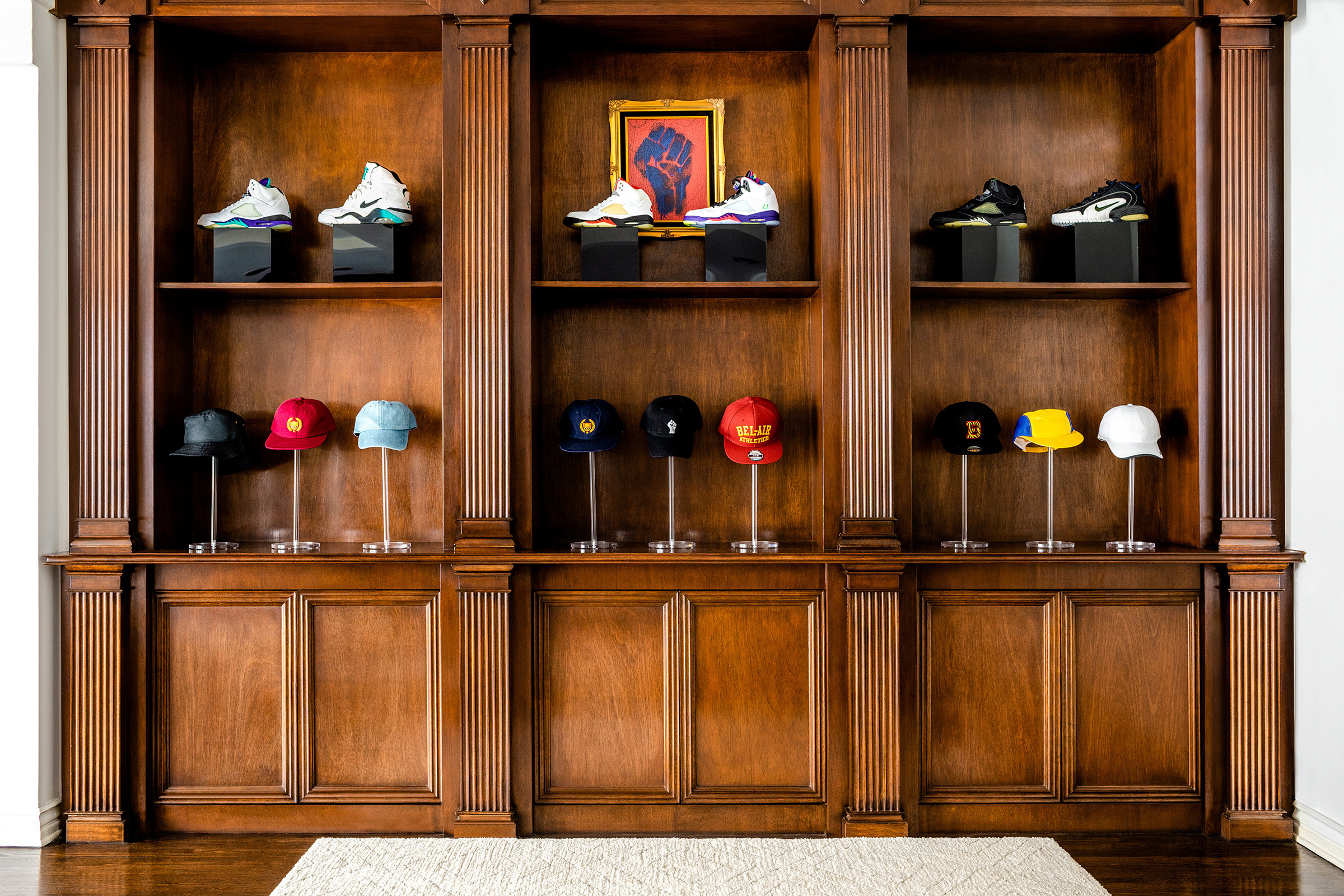 Dark wooden ornate shelving holds fancy sneakers and hats on pedestals 