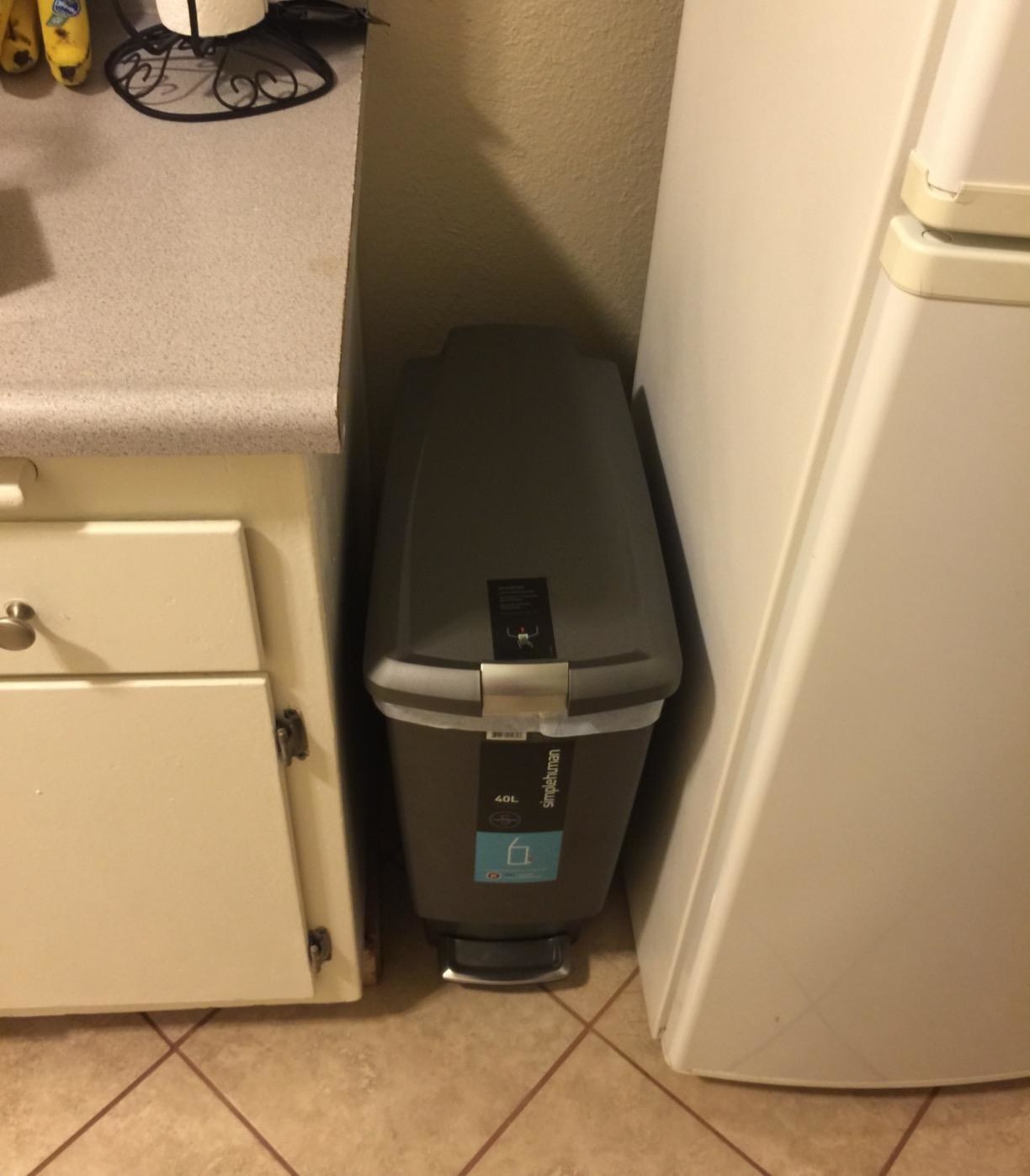 The grey simplehuman Slim Kitchen Step Trash Can in a customer&#x27;s kitchen between their fridge and cabinet