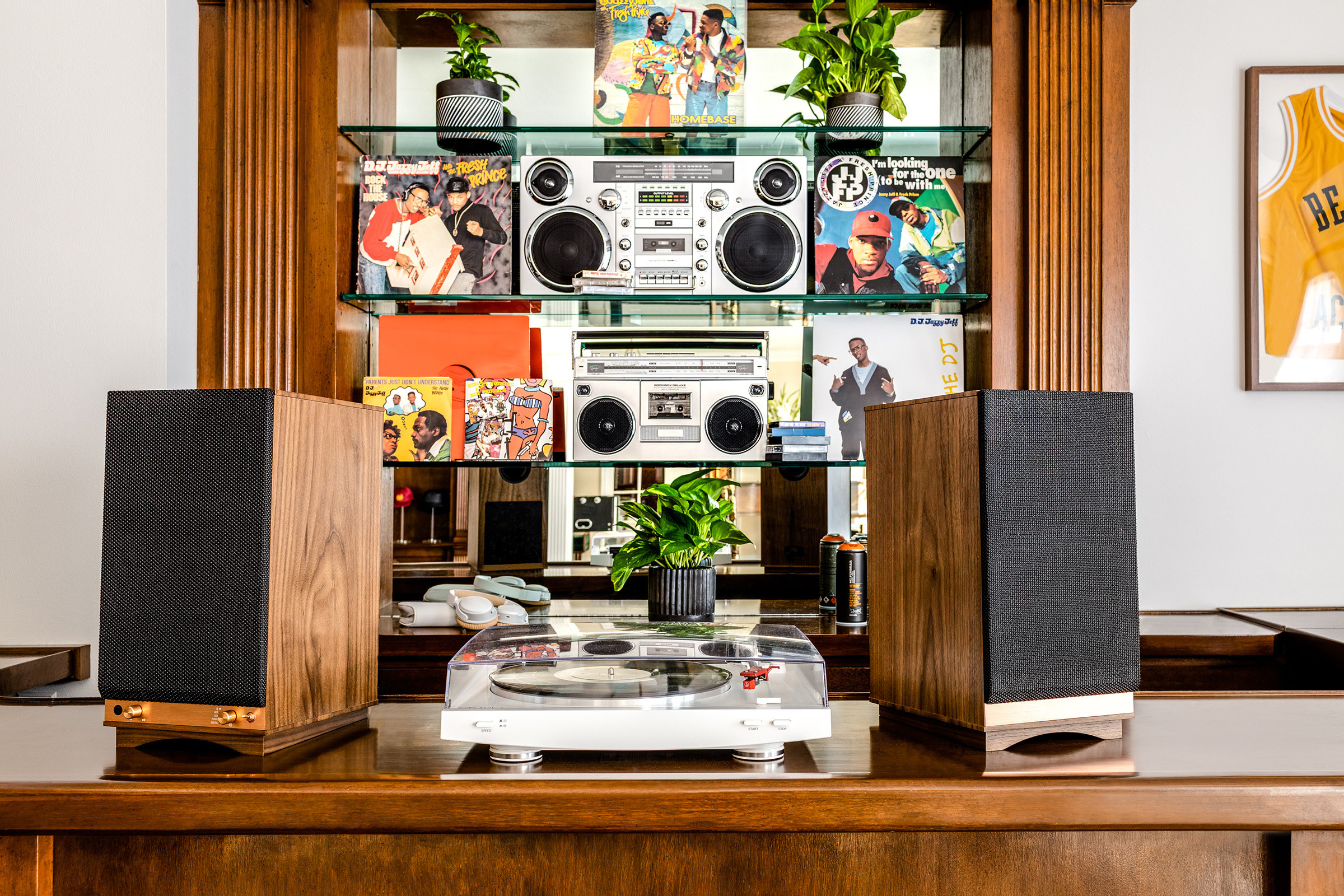 A dark wooden table holds a record player and speakers with shelving of stereos and vinyls behind it