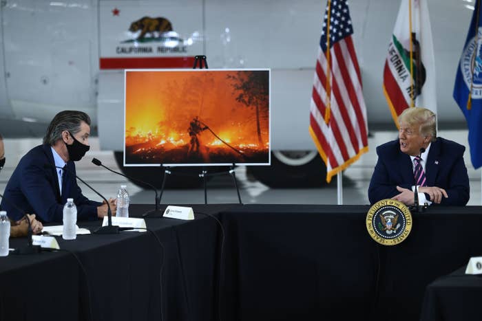 Donald Trump, not wearing a mask, sits at an L-shaped table and speaks with Gavin Newsom, who is wearing a black face mask