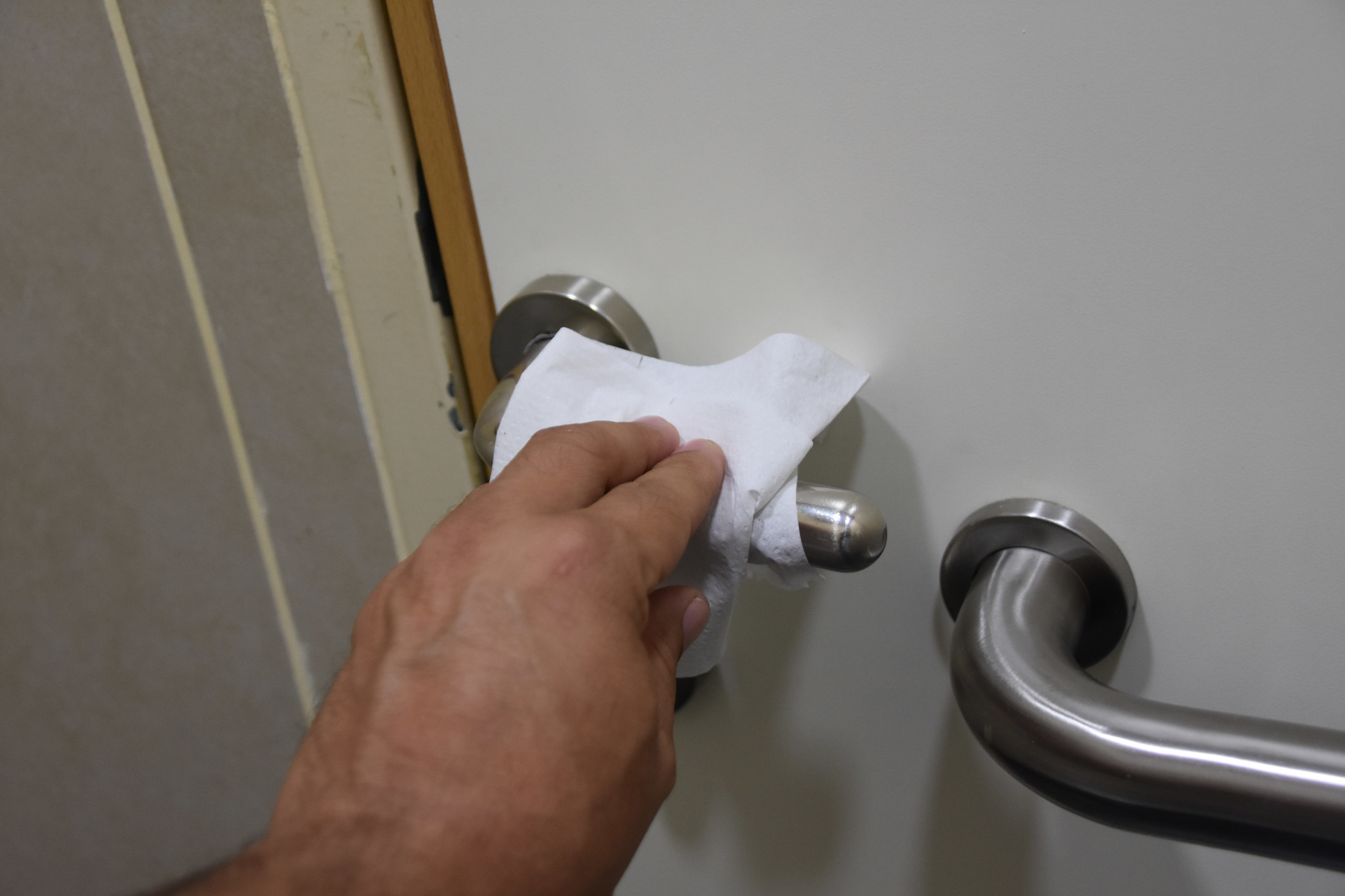 A hand touching a doorknob with a paper towel in hand