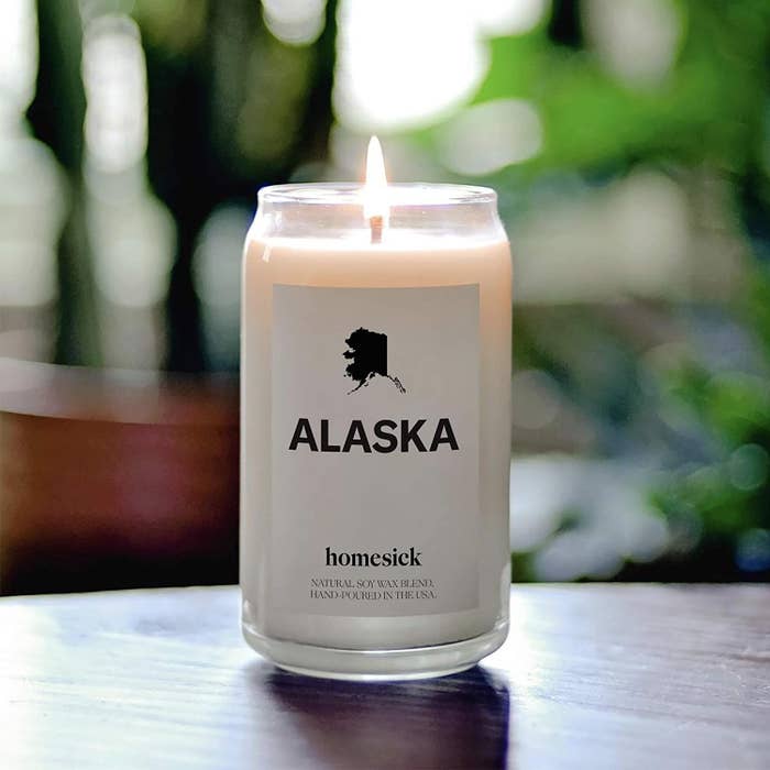 A lit Alaska-scented homesick candle on a tabletop.