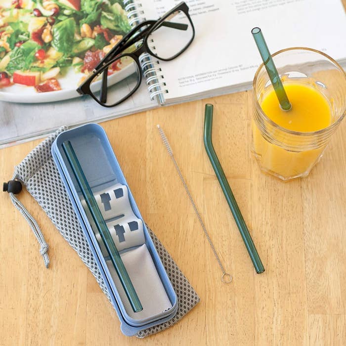 One straw in a drink, one straw and the cleaning brush on a table, and one straw in the case