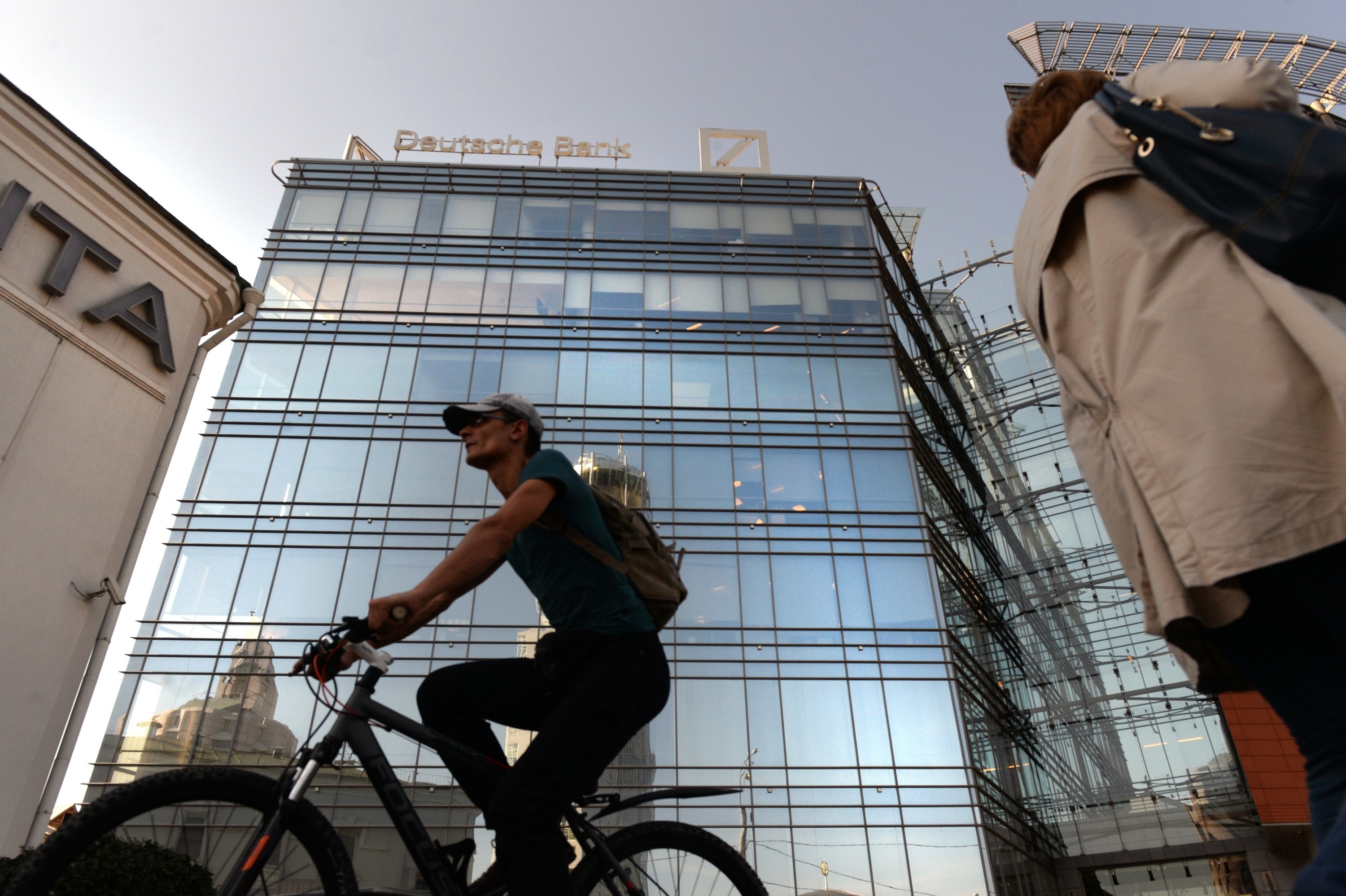 A cyclist rides in front of a towering Deutsche Bank building behind them