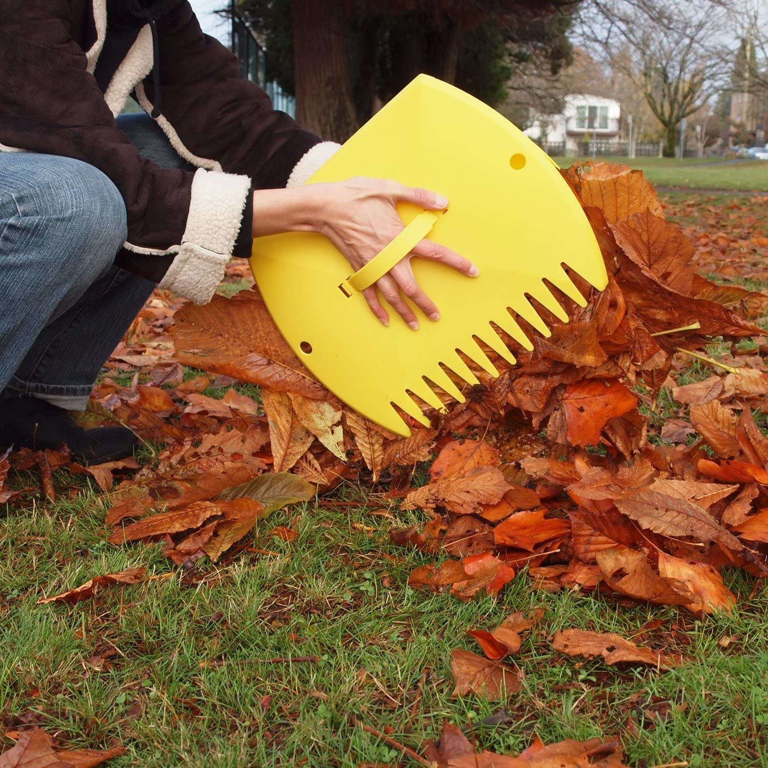 A person picking up a pile of leaves with huge claw-like leaf scoops on their hands