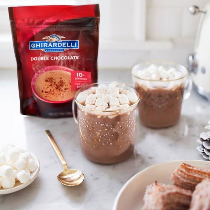 Two glass cups of hot chocolate with marshmallows on top and a small package of hot chocolate mix beside them