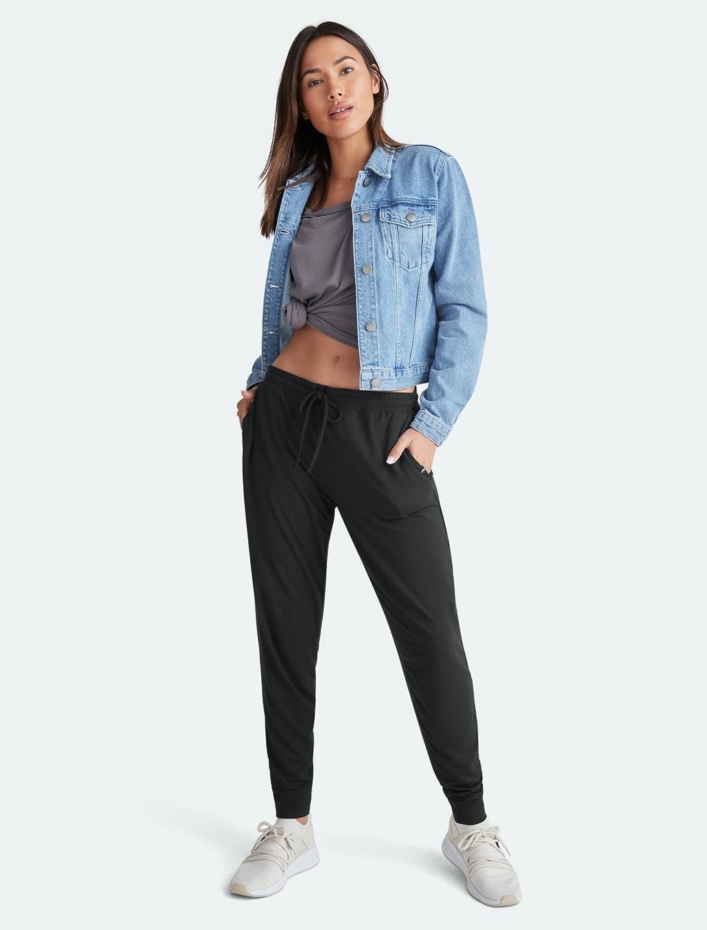 a model wearing black jogger pants with a denim jacket and sneakers