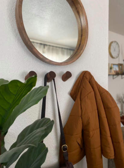 Dark brown wall hooks holding up a black purse and red coat under a mirror