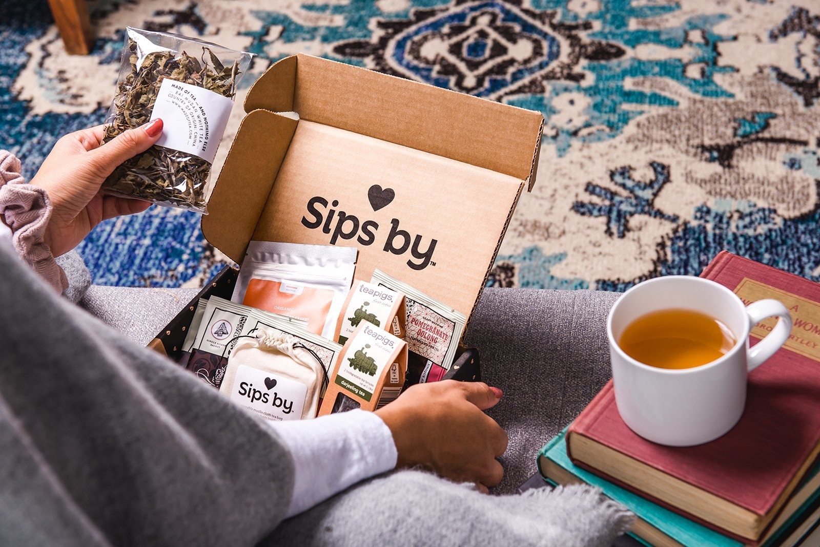 $15/month. a person reaches for their Sips By box which is filled with teas. 