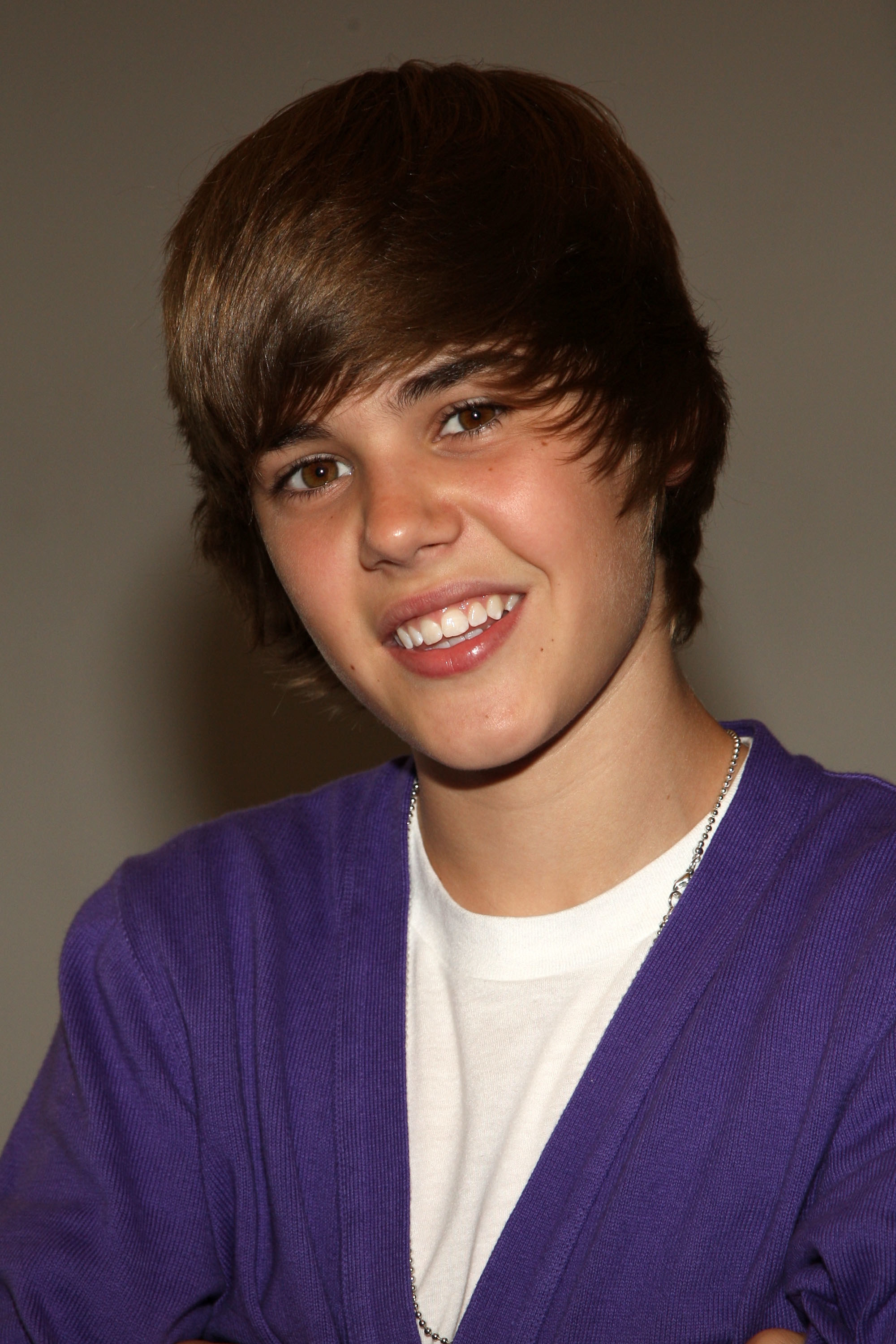 Justin Bieber wearing a dark cardigan and bright t-shirt with a shaggy haircut