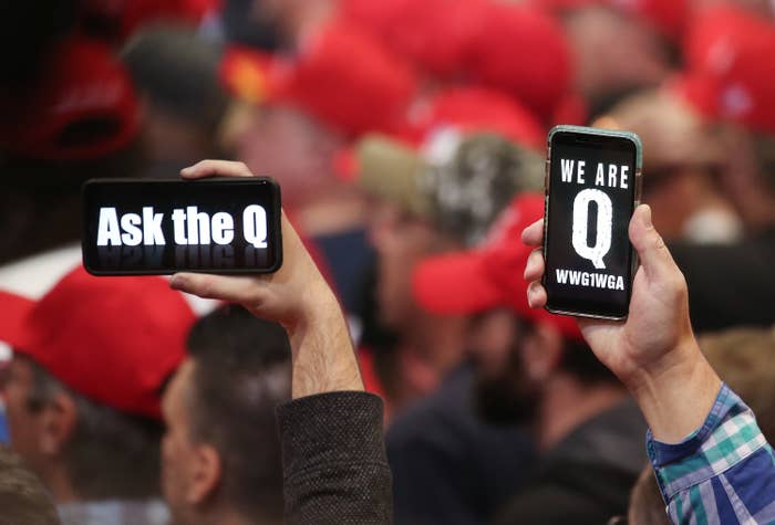 Men hold phones displaying QAnon slogans