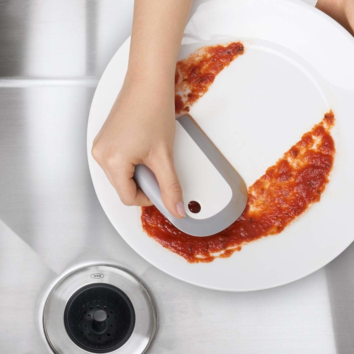 The squeegee and scraper pictured scraping off tomato sauce from a plate.
