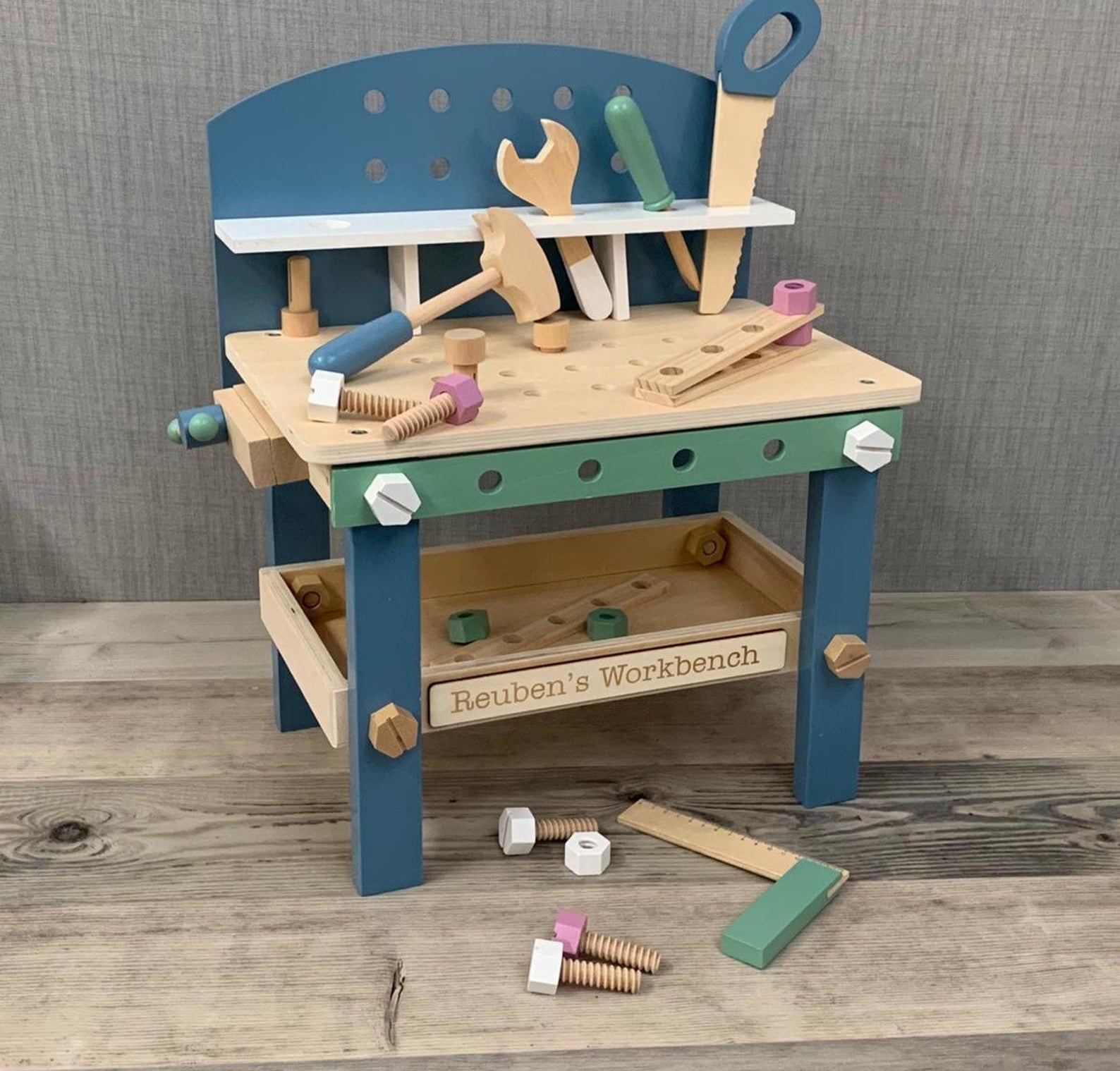 A wooden blue and green toy workbench with various tools