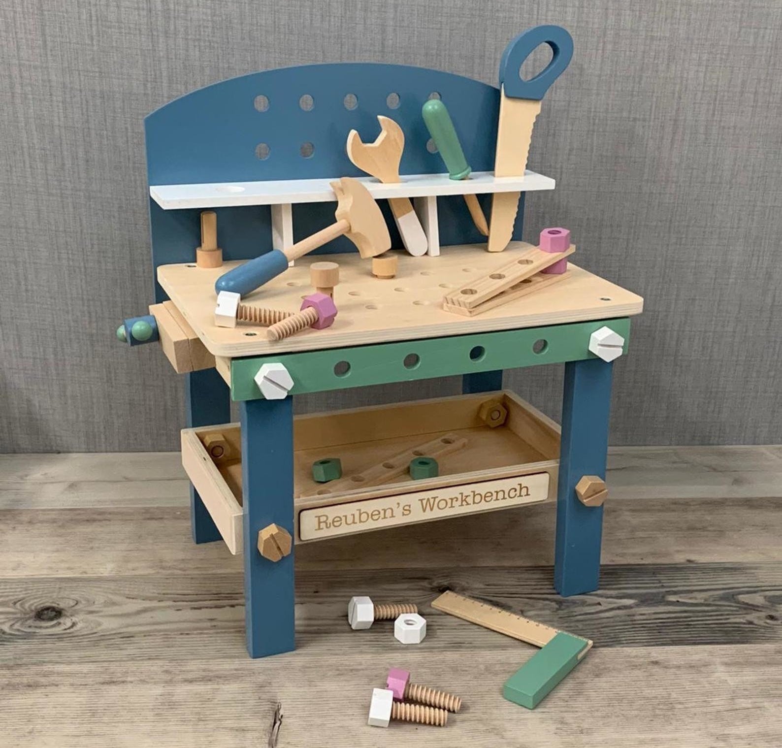 A wooden blue and green toy workbench with various tools