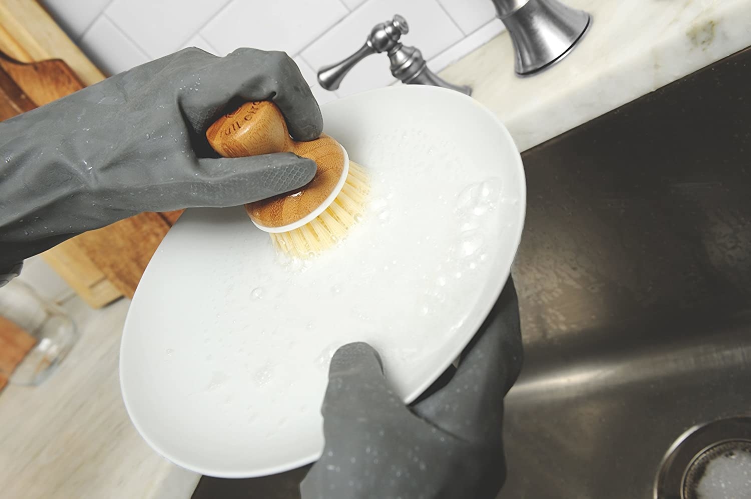 The bamboo-top brush being used to scrub a plate in the sink.