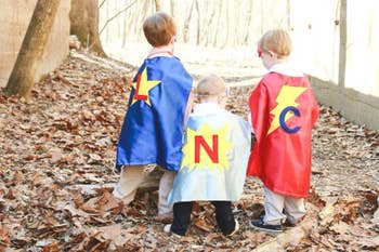 Three child models wearing colorful capes with their first initial on the back 