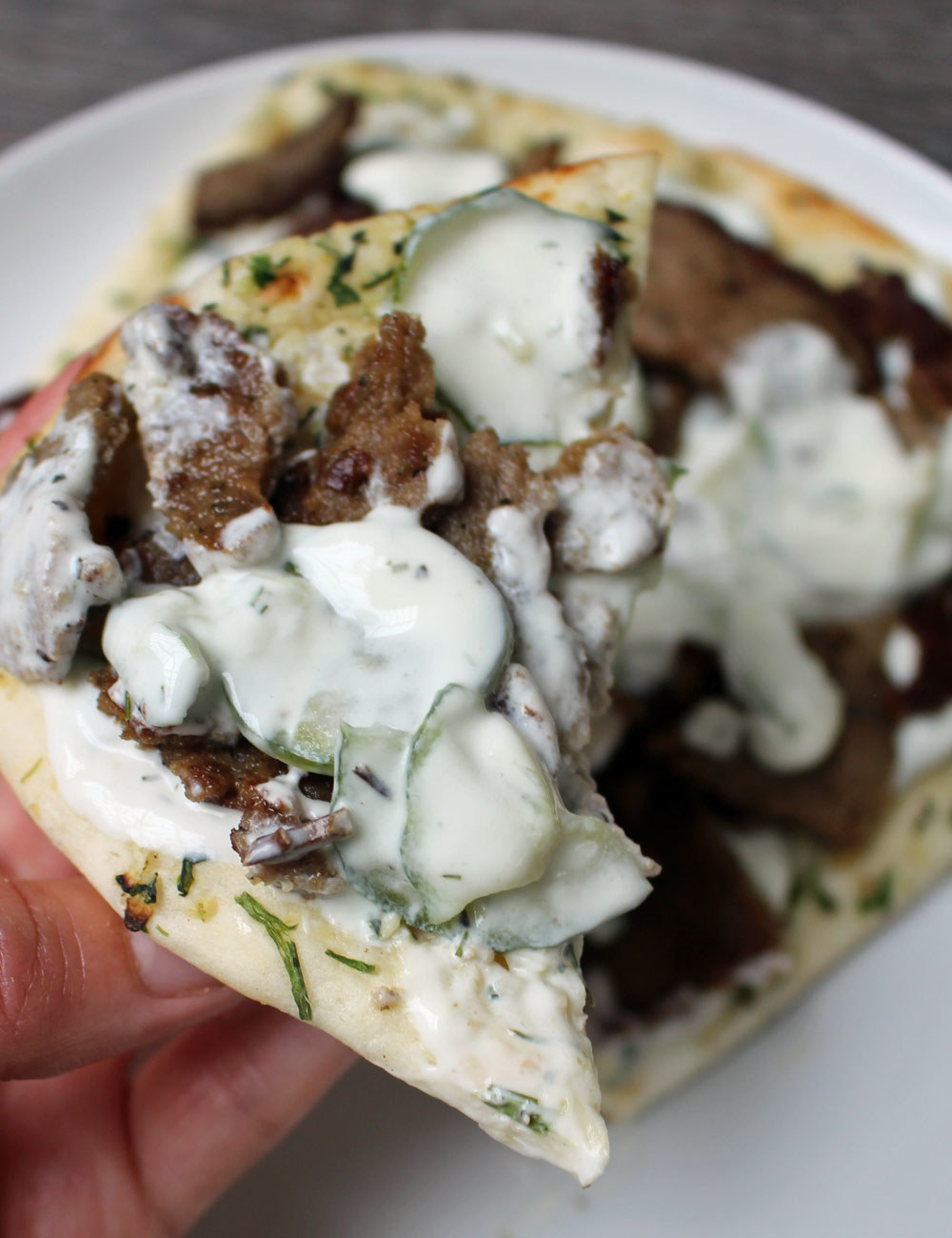 Me holding a slice of naan topped with cucumber tzatziki and sliced gyro.