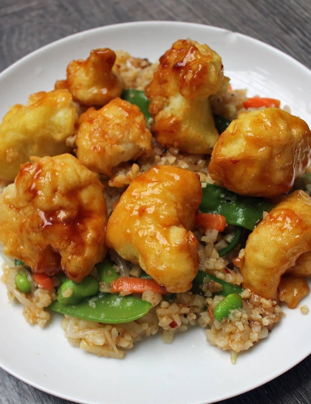 A plate of crispy tempura cauliflower on top of stir fried veggies and cauliflower rice.