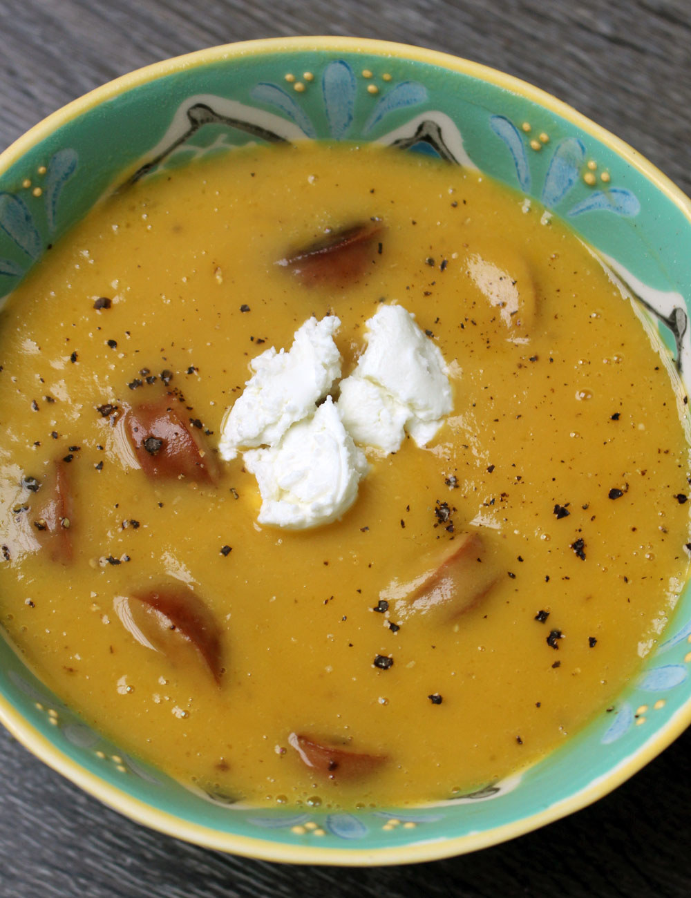 A bowl of butternut squash soup with pieces of sliced chicken sausage and a dollop of goat cheese.