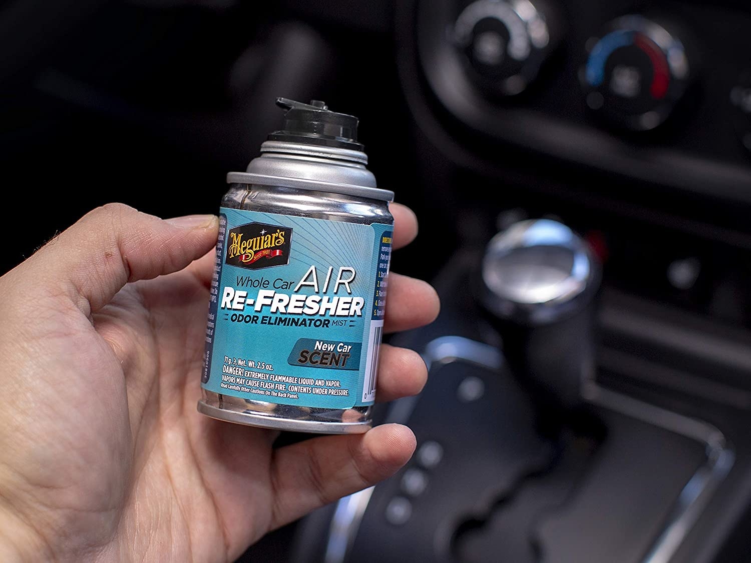 A person holds a small can of the product in a car