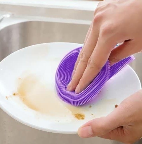 A hand uses a silcone scrubber to get dirt off of a plate