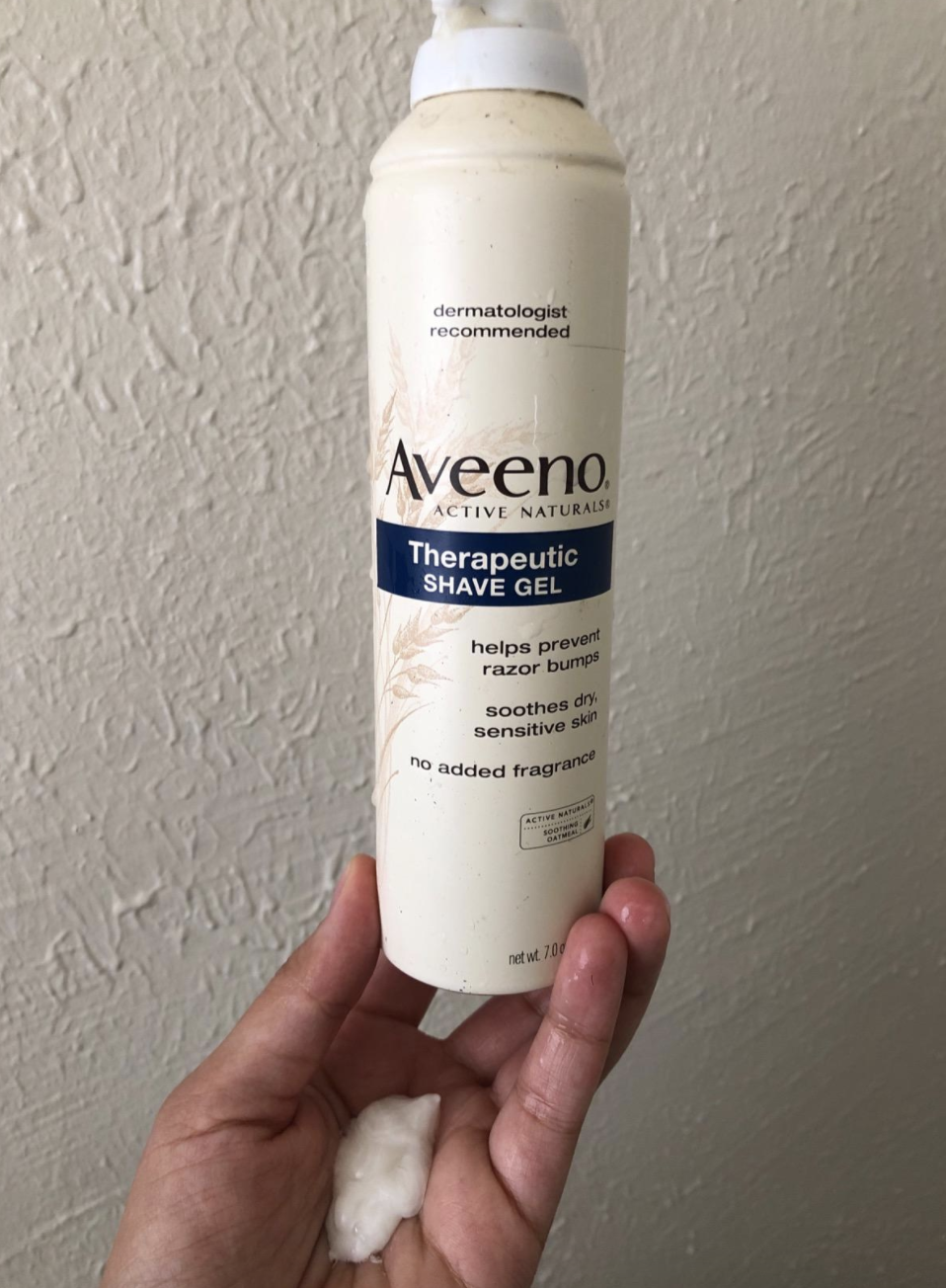 reviewer holding the white bottle labeled &quot;Aveeno therapeutic shave gel&quot;
