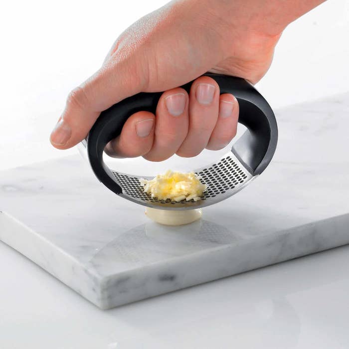 person using a garlic press to mince a garlic clove