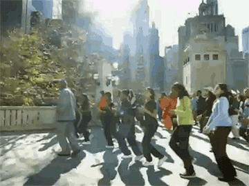A GIF from the music video of  people doing the Cha Cha Slide in a park in New York City 