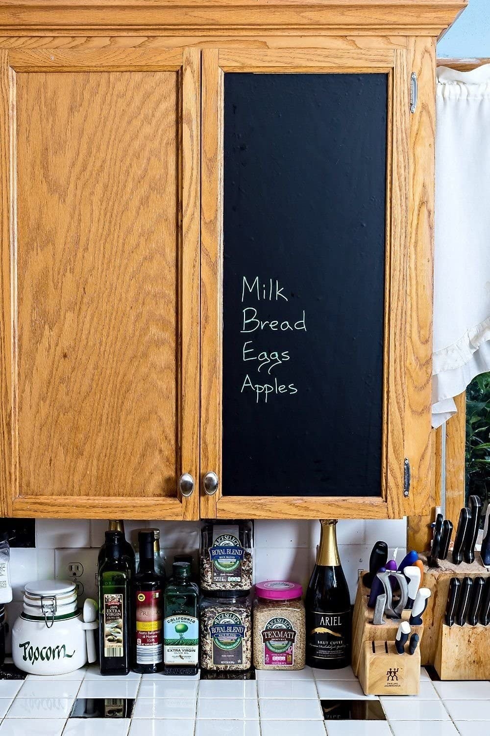 A cabinet door with the chalk adhered to it with milk eggs bread and apples written on it