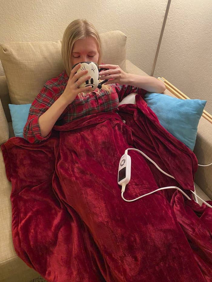 reviewer sitting under the blanket, drinking from a Mickey Mouse mug. Though it does appear she&#x27;s in the &quot;happiest place on earth,&quot; the mug&#x27;s sold separately.