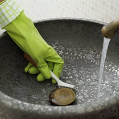 A person wearing rubber gloves cleans around the drain in their sink