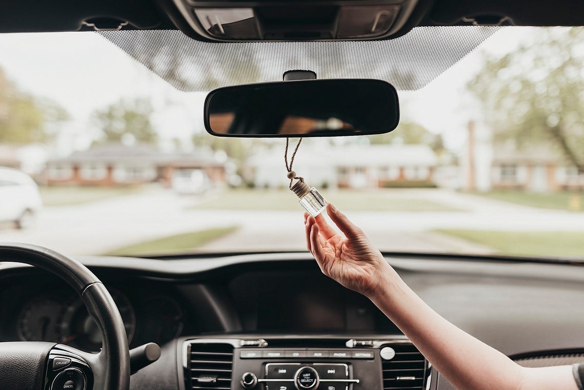 Hand holds small glass container with rope around the rear-view mirror